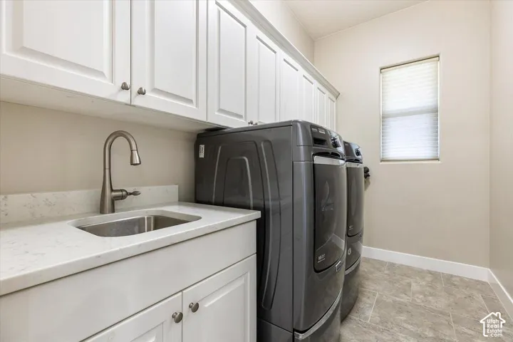 Laundry room featuring expansive white upper cabinetry, a quartz countertop, an undermount stainless steel sink with a high-arch faucet, and tile flooring