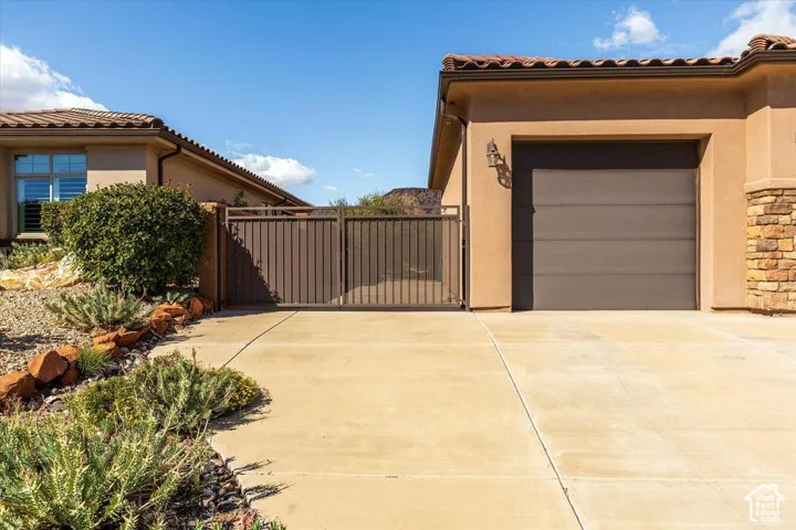 Stucco exterior featuring tile roofing, stone veneer accents, concrete driveway, and metal privacy gate