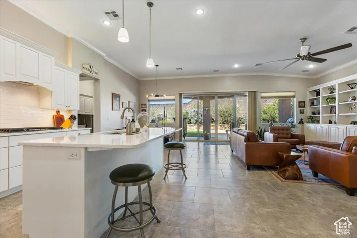 Open-concept floor plan featuring a kitchen island with stone countertops, white cabinetry, tile flooring, and floor-to-ceiling built-in shelving