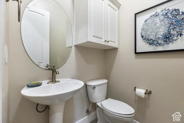 Oval wall-mounted mirror, white pedestal sink with metallic faucet, and white wall-mounted storage cabinetry