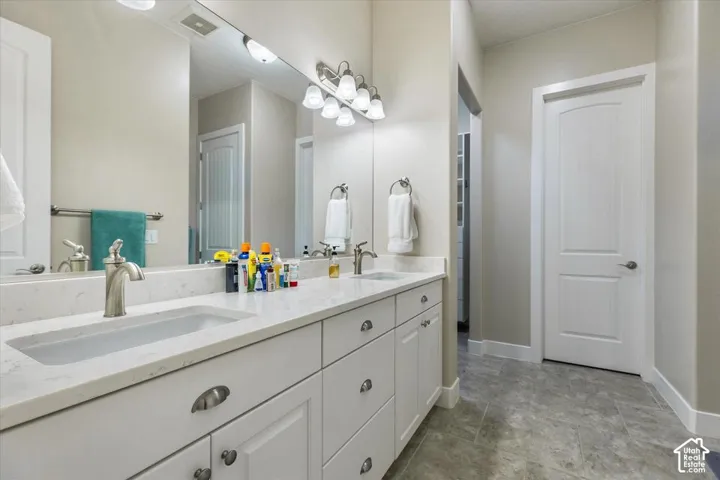 Double vanity with stone-composite countertop, undermount sinks, white shaker-style cabinetry, and tile flooring
