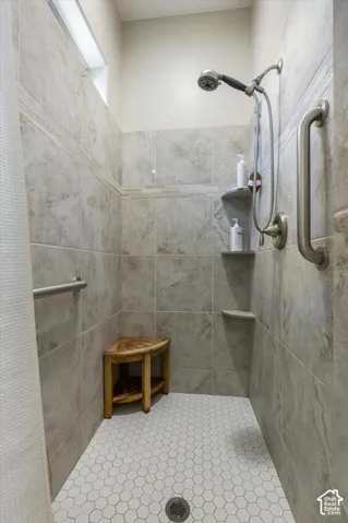 Walk-in shower featuring large-format neutral wall tile, hexagonal floor tile, handheld shower head, and integrated wall-mounted grab bars