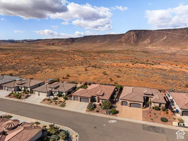 Aerial perspective of a residential neighborhood featuring stucco exteriors, multi-gabled tiled roofing, multi-car garages, and panoramic desert mesa landscape