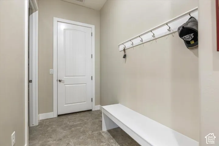 Built-in white storage bench with integrated wall-mounted coat rack featuring multiple metal hooks, contrasted by neutral-toned tile flooring and a solid-core two-panel door