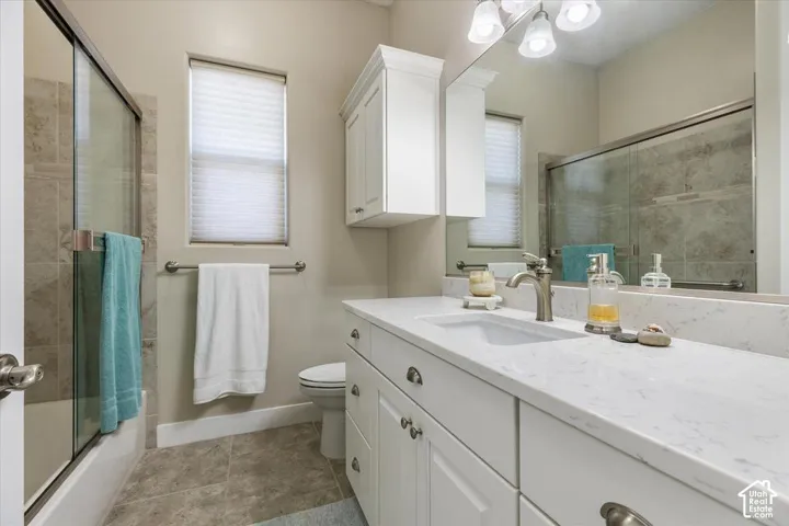 White vanity with stone-look countertop, integrated rectangular sink, wall-mounted storage cabinetry, oversized vanity mirror, and glass-enclosed shower with tile surround