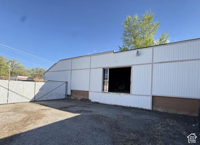 Exterior industrial building featuring vertical metal siding, an elevated loading dock, and a fenced gravel yard