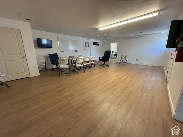 Expansive room featuring wood-finish flooring, smooth-finish walls, and linear LED ceiling lighting