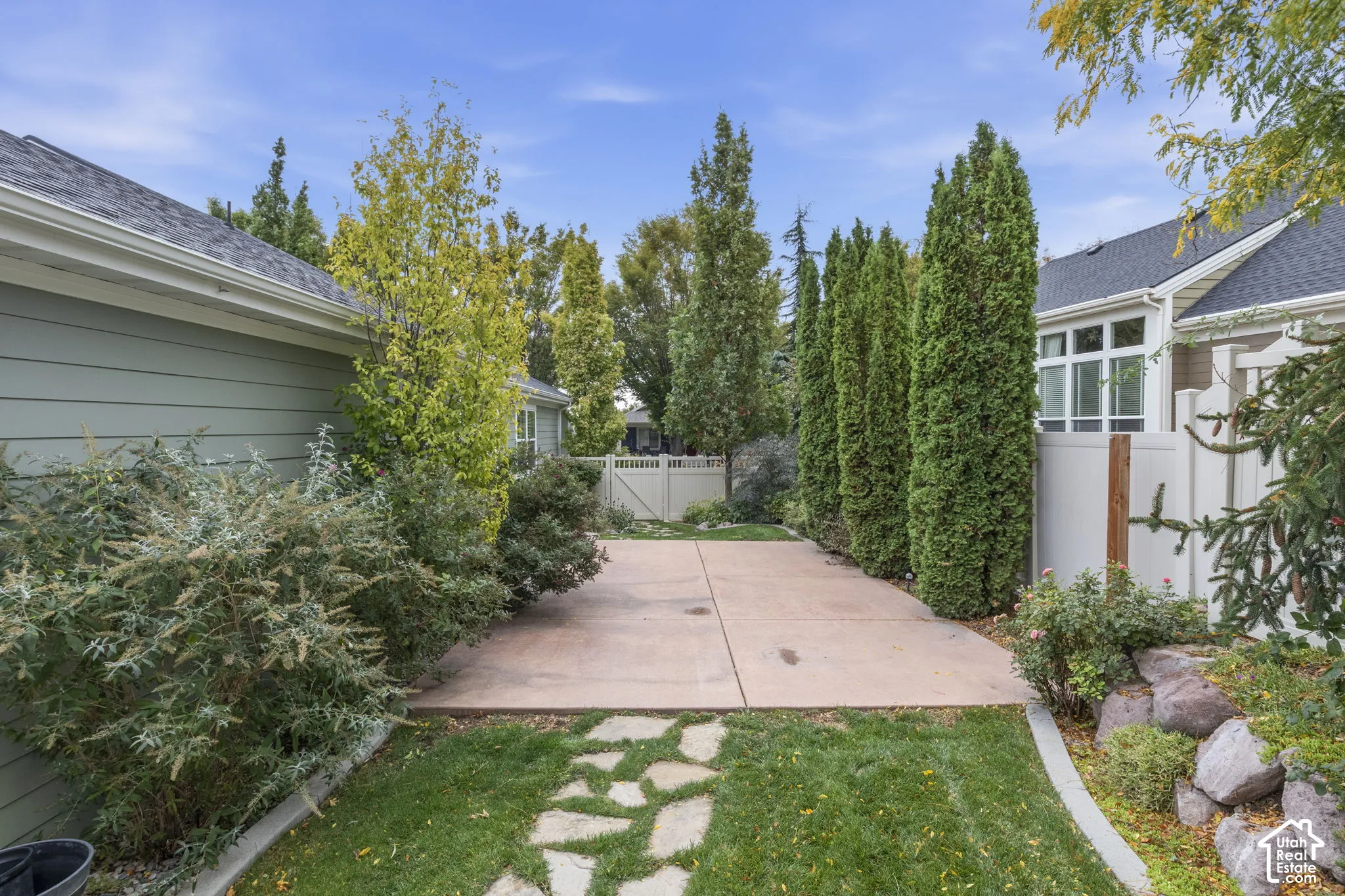 Rear exterior featuring horizontal siding, a concrete patio, stone walkway, tiered rock landscaping, and mature privacy greenery
