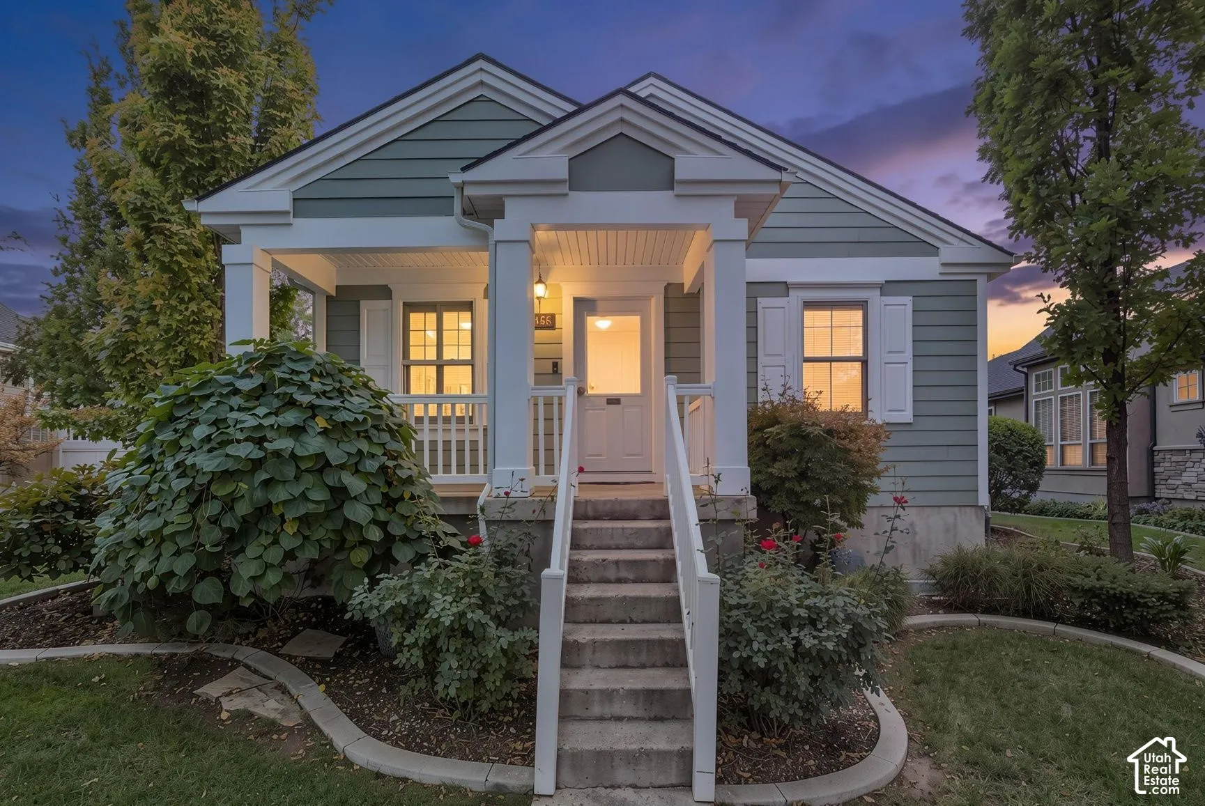 Exterior featuring horizontal lap siding, covered front porch with gable roof, concrete stairs with white railings, and curved landscaping borders