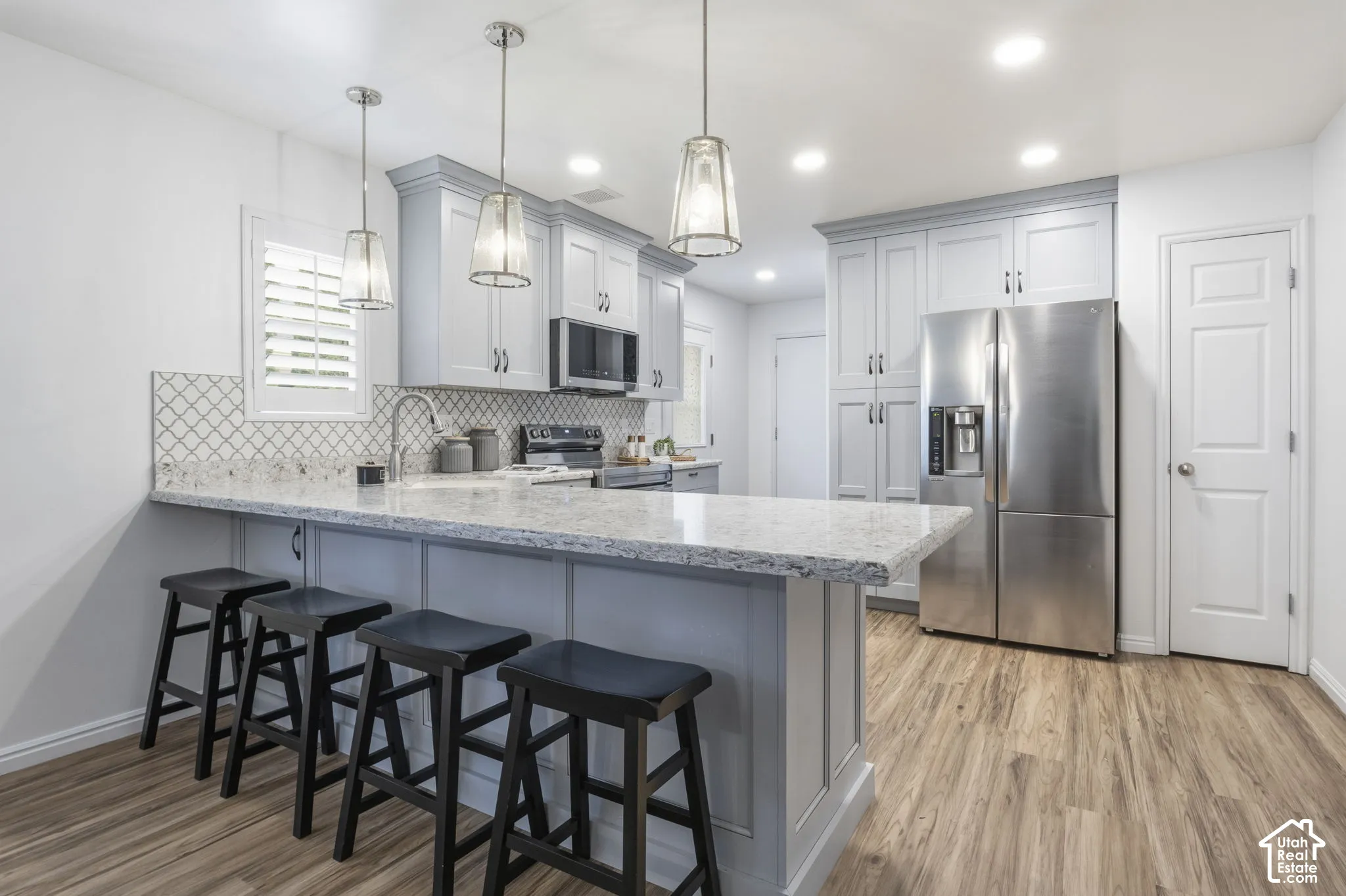 Kitchen featuring light-toned cabinetry, stone-surface countertops with a breakfast bar, stainless steel appliances, patterned tile backsplash, and wood-finish flooring