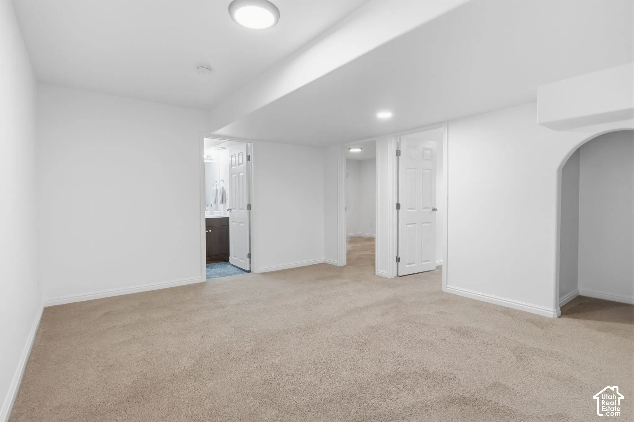 Neutral-toned carpeting, flush-mount lighting, and arched alcove featuring white interior walls and paneled doors