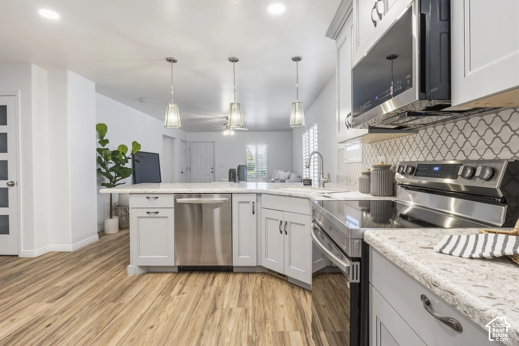 Kitchen featuring shaker-style cabinetry, stone-finish countertops, stainless steel appliances, decorative tile backsplash, and wood-finish flooring