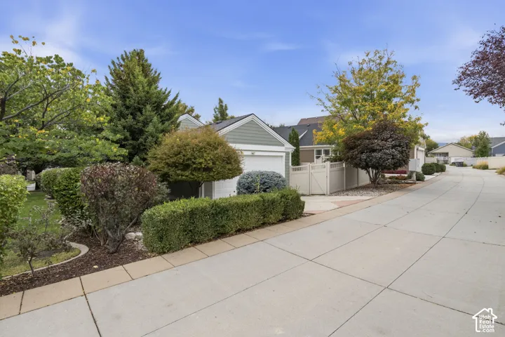 Attached garage featuring horizontal lap siding, a concrete driveway, and professional landscaping with mature trees and shaped shrubbery