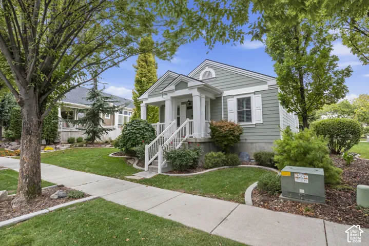 Sage green siding exterior featuring a covered front porch, white column detailing, shuttered windows, and a pediment gable