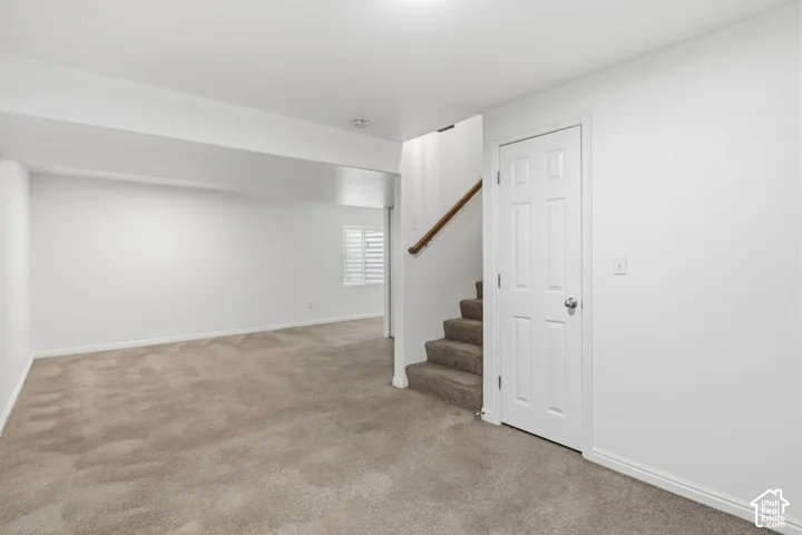 Open-concept interior featuring neutral wall-to-wall carpeting, white walls, shuttered window, and a paneled interior door with a wooden handrail