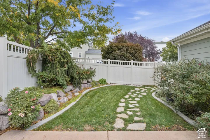 Backyard featuring a stone-paver walkway, manicured lawn, tiered natural rock landscaping, and a tall vinyl privacy fence