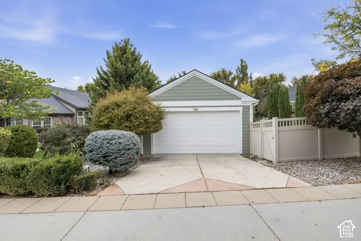 Detached single-car garage featuring horizontal lap siding, a white paneled door, concrete driveway, and vinyl privacy fencing