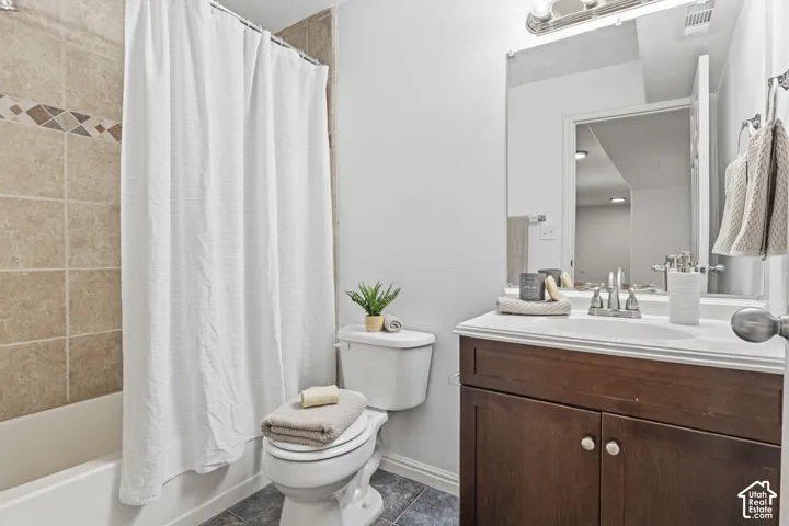 Bathroom featuring a dark wood vanity with a white countertop, wall-to-wall mirror, chrome light fixture, and a tub-shower combination with decorative tile inlay