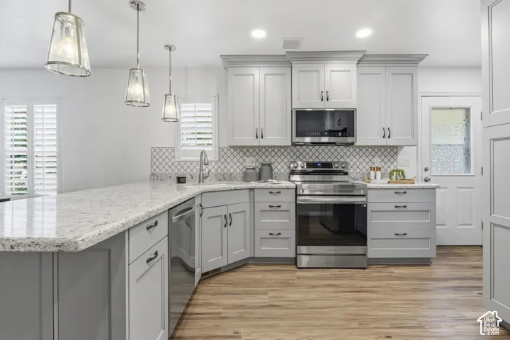 Kitchen featuring light grey Shaker-style cabinetry, stone countertops, diamond-patterned backsplash, stainless steel appliances, and pendant lighting