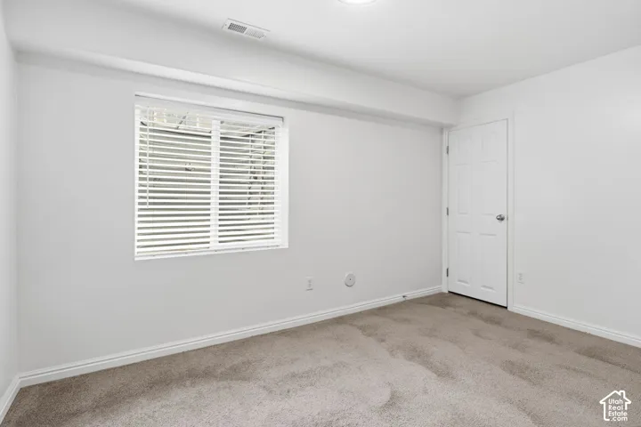 Neutral-toned carpet flooring, white walls, six-panel interior door, and horizontal window blinds
