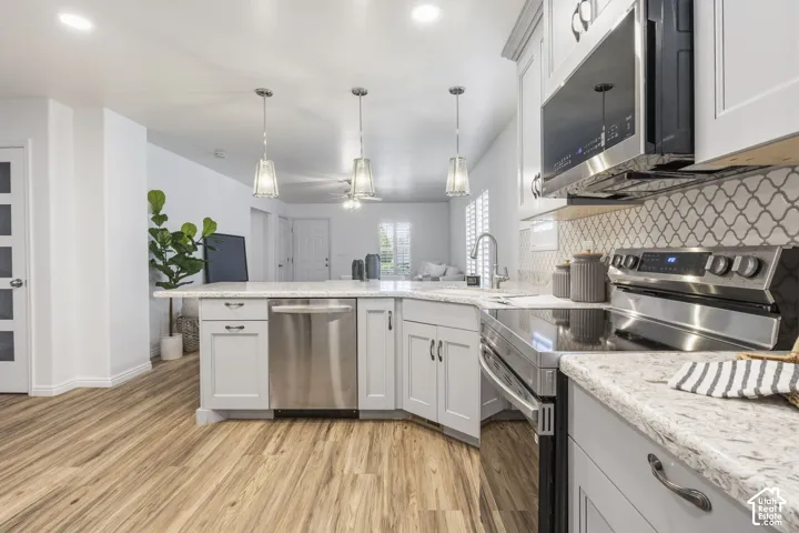 Kitchen featuring shaker-style cabinetry, stone-finish countertops, stainless steel appliances, decorative tile backsplash, and wood-finish flooring