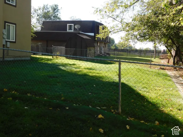Fenced backyard featuring a manicured lawn, perimeter chain-link fencing, and mature trees