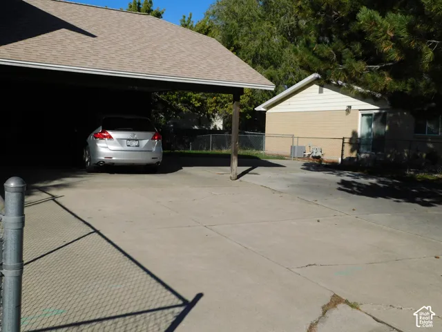 Concrete driveway with a covered carport, chain-link fencing, and exterior brick siding