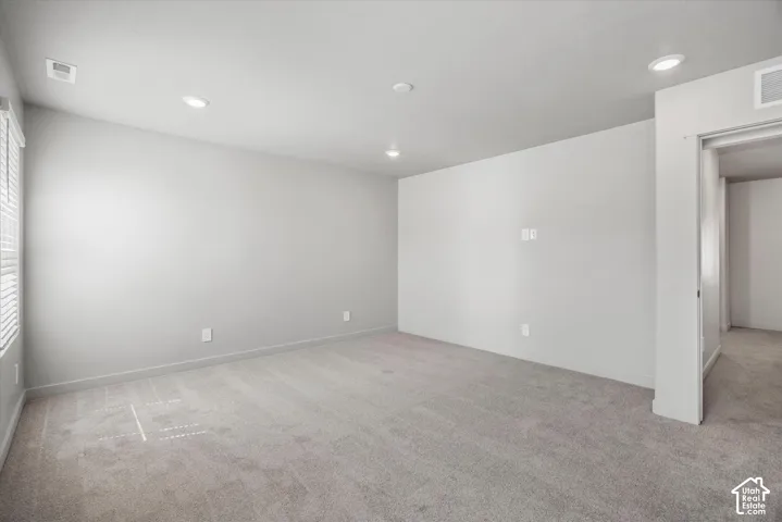 Neutral-toned room featuring wall-to-wall carpeting, recessed ceiling lighting, and a window with horizontal blinds