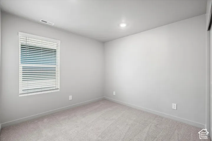 Neutral-toned interior space featuring light-colored wall-to-wall carpeting, recessed ceiling lighting, and a window with horizontal blinds