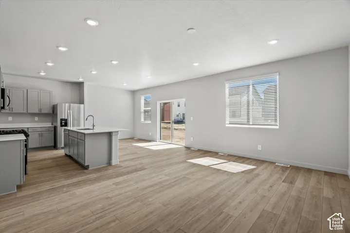 Open-concept kitchen featuring gray cabinetry, a central island with a stone-surface countertop, recessed lighting, and wood-finish flooring