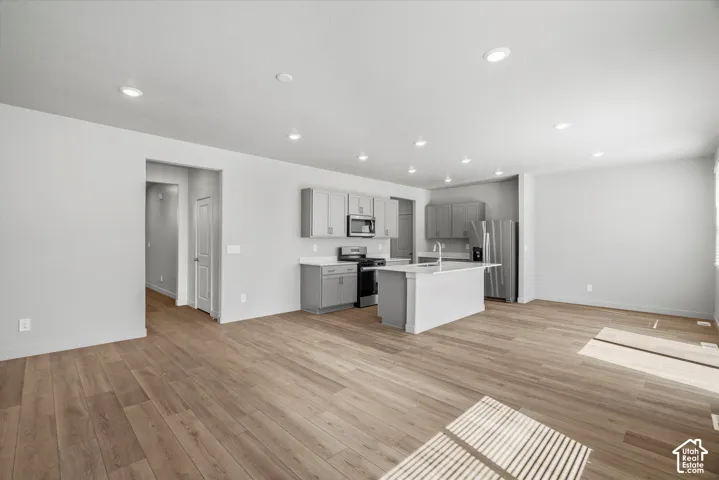 Kitchen featuring gray cabinetry, quartz countertops, a central island with a sink, recessed lighting, and wood-finish flooring