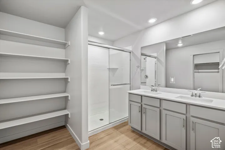 Double vanity featuring a light-toned countertop with integrated rectangular sinks, grey cabinetry, wood-finish flooring, glass-enclosed shower, and built-in wall shelving