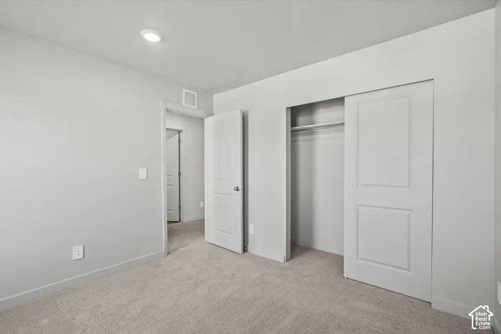 Neutral-toned interior space featuring neutral wall-to-wall carpeting, crisp off-white wall finishes, recessed ceiling lighting, and a closet with a two-panel sliding door