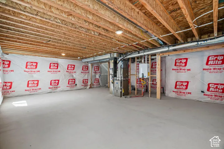 Unfinished basement featuring exposed joist ceilings, concrete flooring, vapor barrier wall insulation, and a wall-mounted tankless water heater