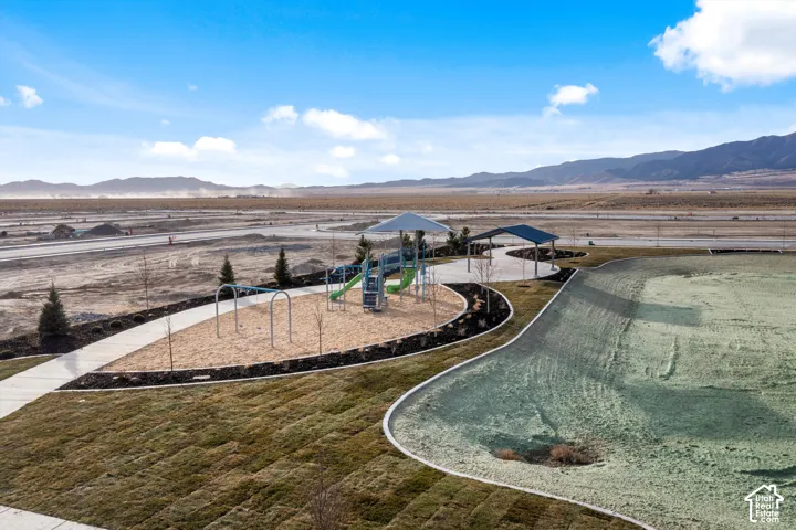 Community park featuring a playground, shaded pavilion, paved walking paths, and expansive open green space, set against a mountain backdrop