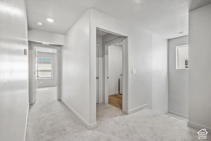 Neutral interior hallway featuring light-toned carpeting, recessed lighting, and crisp white wall finishes