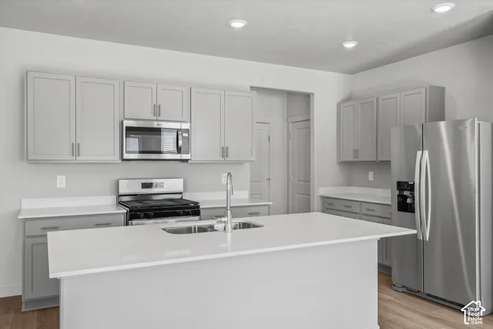 Kitchen featuring shaker-style cabinetry, a central island with a double-basin stainless steel sink, stone-finish countertops, stainless steel appliances, and recessed lighting