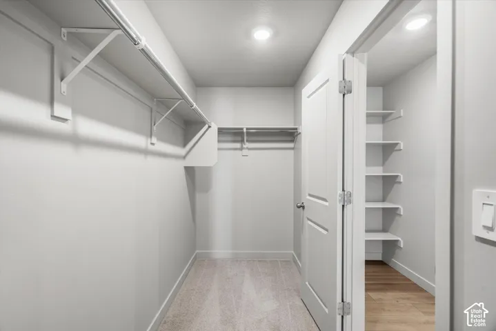 Walk-in closet featuring wall-to-wall carpeting, white metal shelving, and an integrated auxiliary storage room with built-in wooden shelving