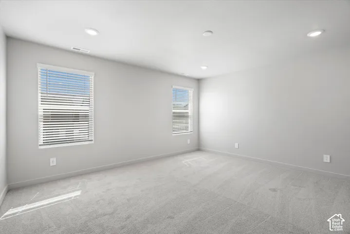 Neutral-toned interior featuring wall-to-wall carpeting, recessed ceiling lighting, and dual windows with fitted blinds
