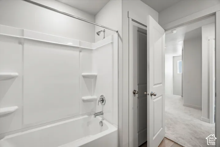 Full bathtub enclosure with integrated shelving, metallic finish showerhead and faucet, white panel doors, and neutral carpeting