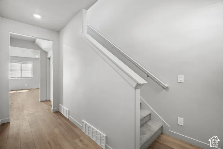 Staircase featuring a painted wood handrail, neutral carpeting on the steps, wood-finish flooring, and recessed ceiling lighting