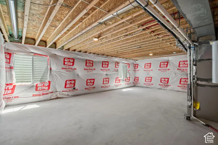 Unfinished lower-level space featuring concrete flooring, exposed wooden joist ceiling, and two windows
