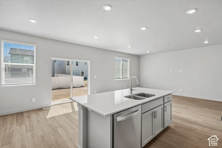 Kitchen island featuring a stone-surface countertop, dual-basin stainless steel sink, pull-down faucet, and neutral-toned cabinetry, complemented by wood-finish flooring and recessed lighting