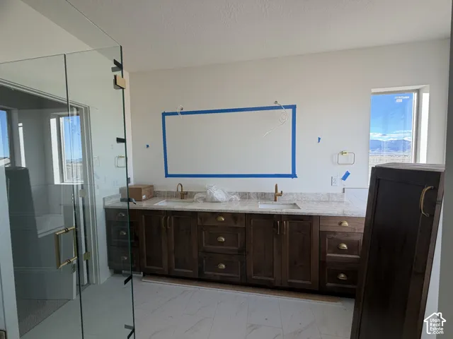 Double vanity with stone-finish countertop, undermount sinks, brass-toned hardware, and a frameless glass-enclosed shower with tile flooring
