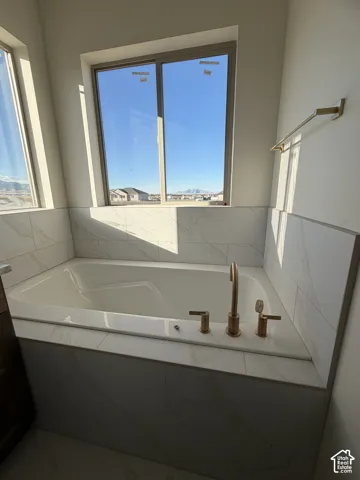 Built-in soaking tub surrounded by large-format tile with stone-pattern veining, featuring gold-tone fixtures and a wall-mounted towel bar