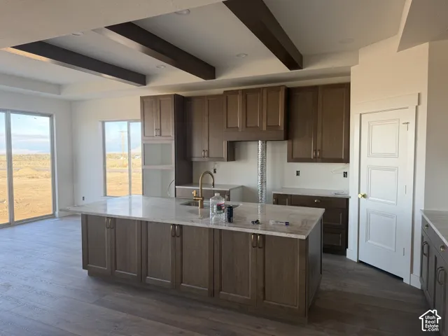 Kitchen featuring wood-finish cabinetry, an oversized center island with stone countertop, wood-finish flooring, and exposed ceiling beams