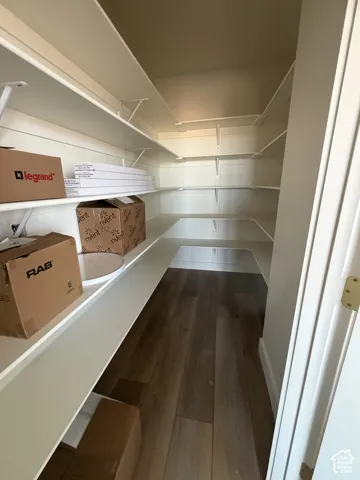 Walk-in storage space featuring multi-tiered white shelving and wood-finish flooring