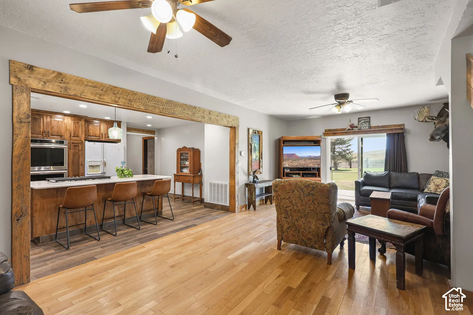 Open-concept interior featuring prominent rough-hewn timber ceiling beams, hardwood flooring, a kitchen island with a stone countertop, and glass sliding doors