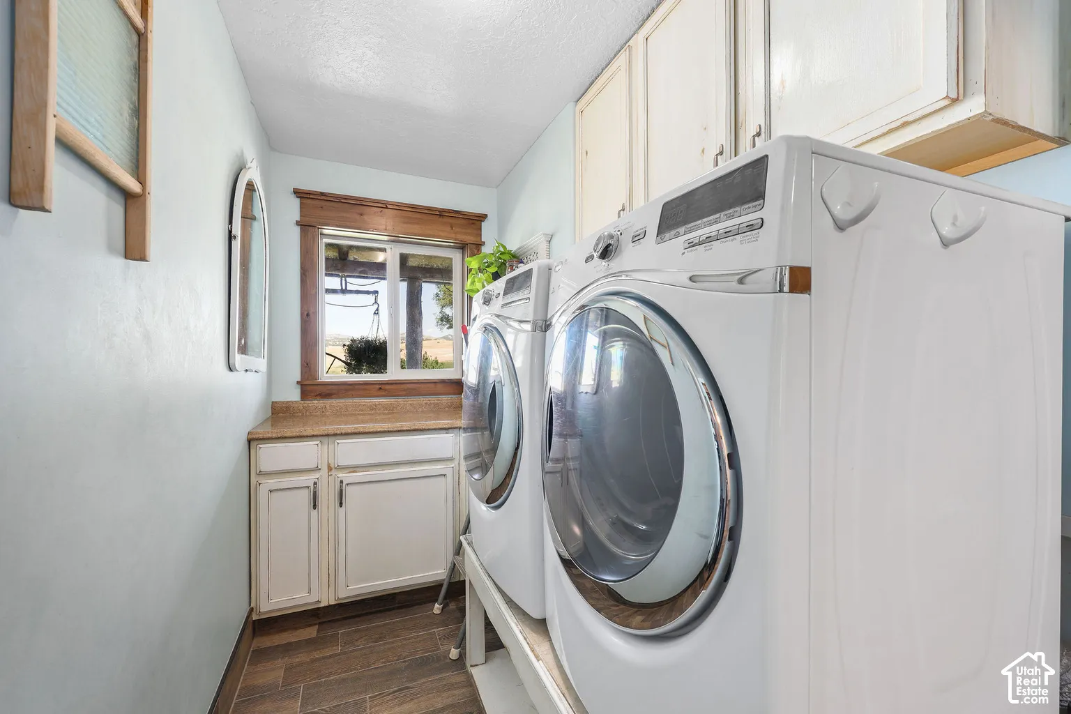 Laundry room featuring wood-finish tile flooring, shaker-style cabinetry, solid-surface countertops, and wood-trimmed window casing