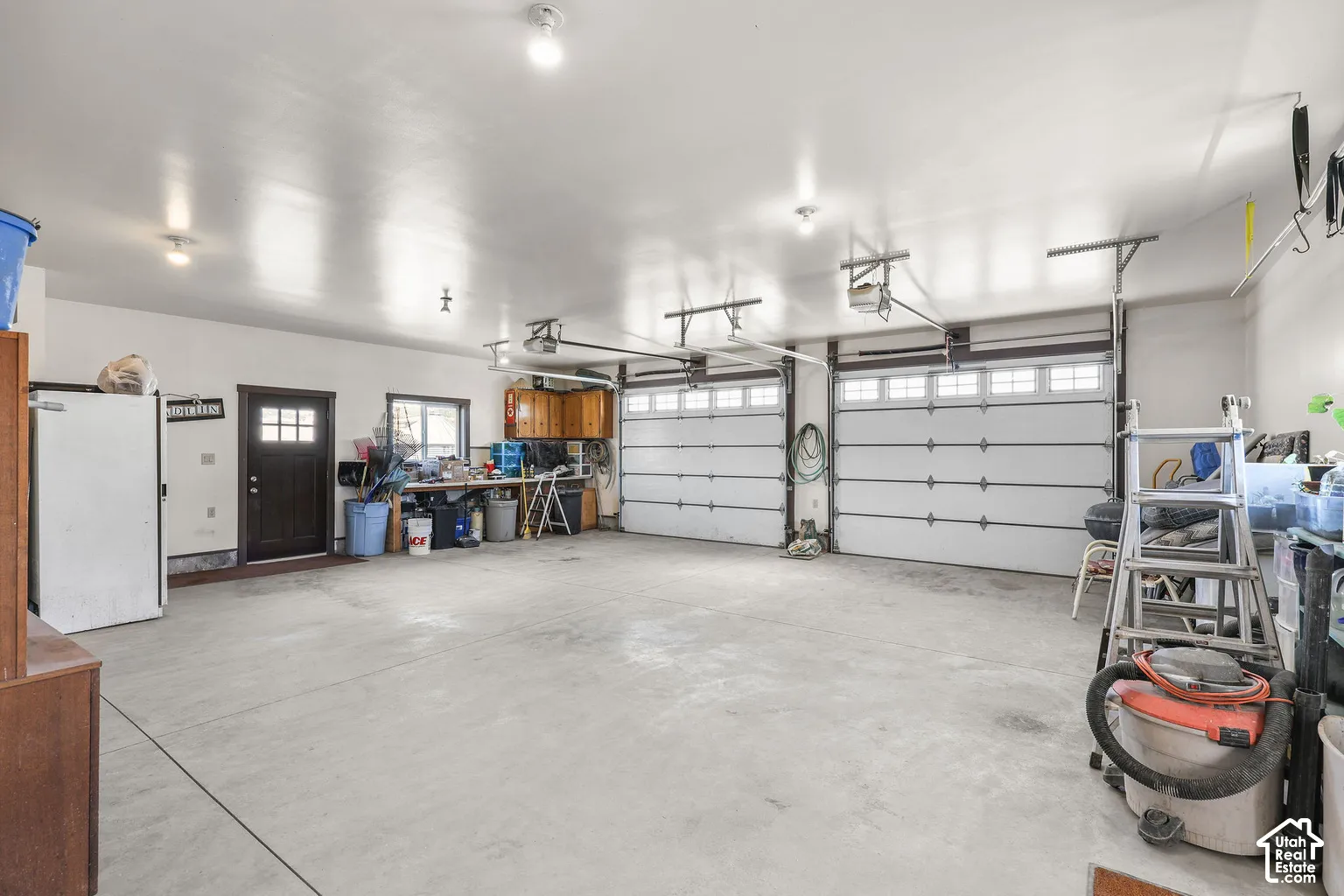 Three-car garage featuring two overhead doors, concrete flooring, built-in wooden cabinetry, and an exterior access door with glass panes